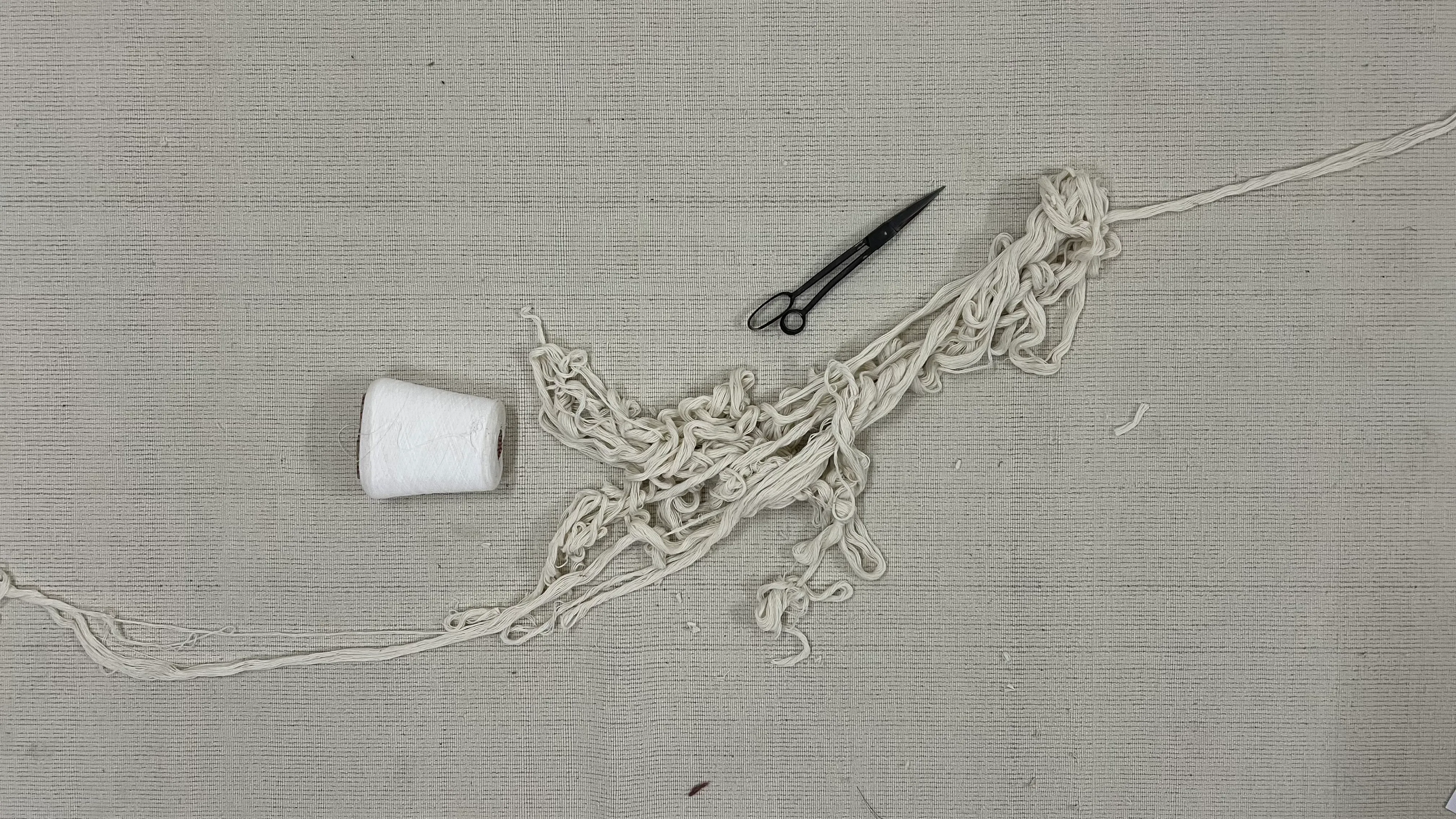 Scissors, thread, and hand-knotted yarn ends on undyed mill cloth
