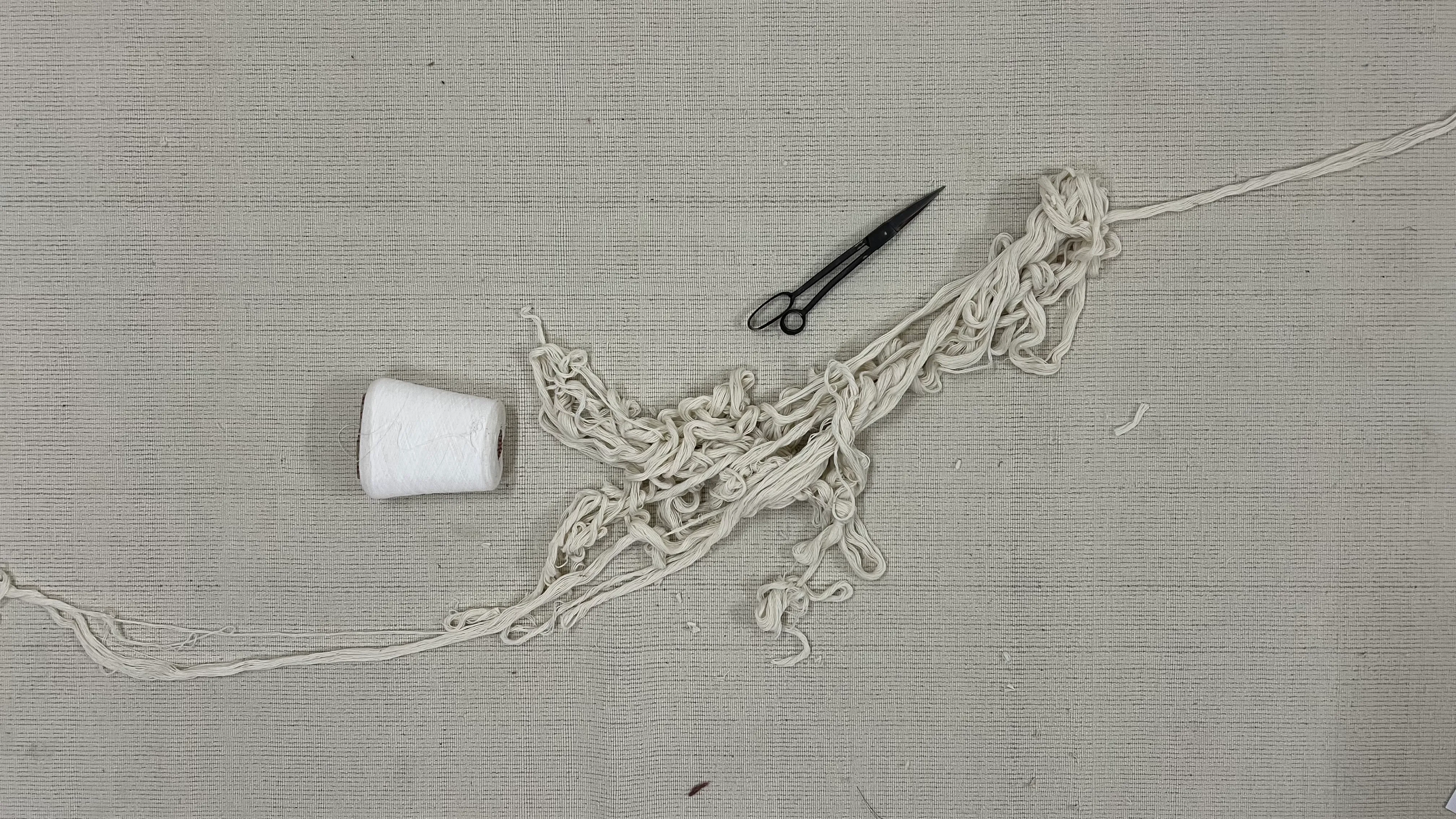 Scissors, thread, and hand-knotted yarn ends on undyed mill cloth